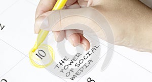 Hand encircles a date on a calendar with text THE POWER OF SOCIAL MEDIA yellow felt-tip pen