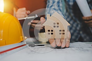 Hand of engineer and architect showing house model and working on blueprint on desk
