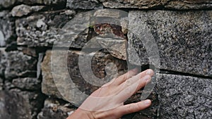 The hand exploration the stone surface of the wall, picks the stone, studies the structure of the wall.
