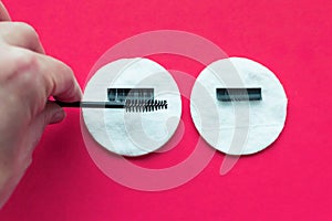 The hand of the eyelash extension master combs artificial eyelashes with a brush on a cotton swab on a pink background