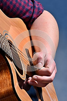 Hand of female guitarist striking strings on acoustic guitar with pick