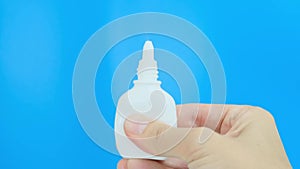 Hand, fingers pushing white plastic nasal spray against blue background - sinusitis, geniantritis, rhinitis and other