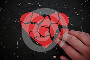 Hand fixing and repairing a broken red heart paper cutout in black background.