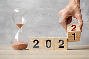 Hand flipping block 2021 to 2022 text with hourglass on table. Resolution, time, plan, goal, motivation, reboot, countdown  and