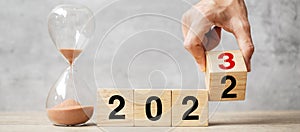 Hand flipping block 2022 to 2023 text with hourglass on table. Resolution, time, plan, goal, motivation, reboot, countdown  and