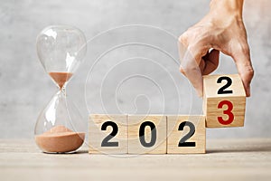 Hand flipping block 2022 to 2023 text with hourglass on table. Resolution, time, plan, goal, motivation, reboot, countdown  and