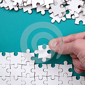 The hand folds a white jigsaw puzzle and a pile of uncombed puzzle pieces lies against the background of the blue surface. Texture