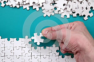 The hand folds a white jigsaw puzzle and a pile of uncombed puzzle pieces lies against the background of the blue surface. Texture