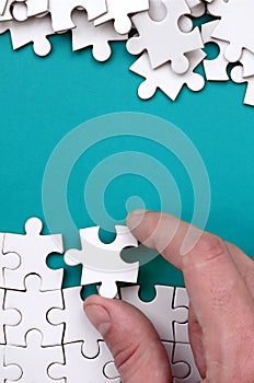 The hand folds a white jigsaw puzzle and a pile of uncombed puzzle pieces lies against the background of the blue surface. Texture