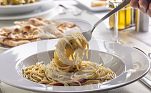 Hand with a fork spinning spaghetti aglio e olio peperoncino from a plate in a restaurant photo