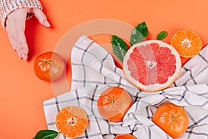 Hand with fresh ripe mandarins and grapefruit with green leaves on white towel on orange background