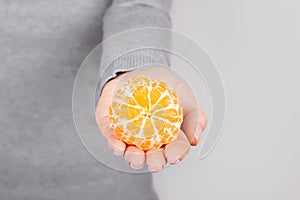 Hand with fresh tangerine on grey background