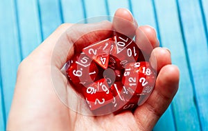 Hand full of red polyhedral RPG board game dice, closeup. Man holding a heap of stylish game dice, lots of dice used for rpg