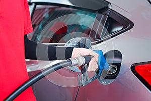 Hand of gas station attendant holding a fuel petrol pump nozzle against for filling up the car with petrol at gas station