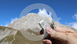 hand of the geologist holding a clear stone and the mountain cal