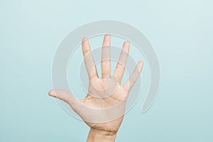 Hand gesture. Female hand shows number five. Woman hand pointing up with three fingers on light blue background