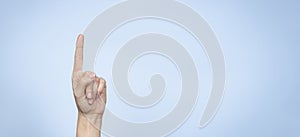 Hand gesture. Female hand shows number one. Woman pointing up with index finger on light blue background