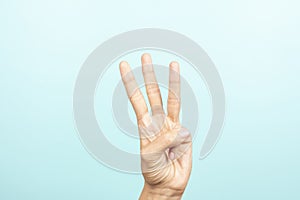 Hand gesture. Female hand shows number three. Woman hand pointing up with three fingers on light blue background