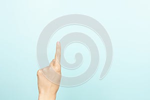 Hand gesture show, touch, index, press, select something. Woman pointing up with index finger on light blue background