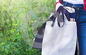 Hand of girl holding eco cloth canvas fabric bags and paper bag for organic shopping. Nature green background. Zero waste.