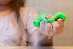 Hand of a girl holding a green slime. Slime in hand close-up. The child plays a slime, stretches it. Creative toy for