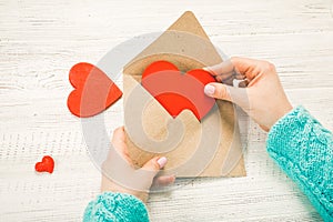 Hand of girl writing love letter on Saint Valentines Day. Handmade postcard with red heart shaped figure. 14 February holiday