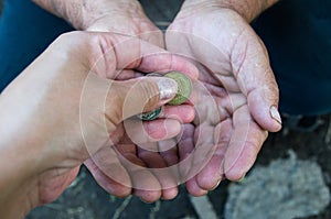 The hand gives a coin to the hands of the old man. Elderly man with a coin in his hands. Poverty in old age. Alms concept.