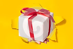 Hand giving gift box through torn yellow paper background, closeup. Special offer or sale concept