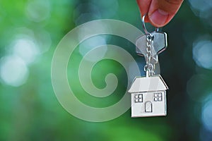 Hand giving home key with love house keyring with blur green garden, background, sweet home concept