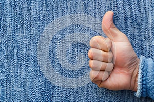 A hand giving a thumbs up on a blue fabric background