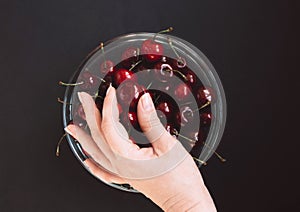 Hand on a glass bowl with juicy and red cherries