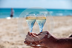 Hand with glass of cava or champagne sparkling wine on vacation, Dunes Corralejo sandy beach, Fuerteventura, Canary islands, blue