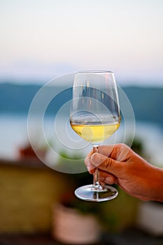 Hand with glass of cold dry white wine served outdoor in cafe at night in Italy