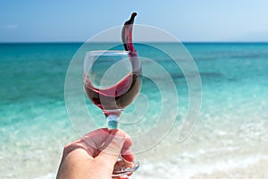 Hand with glass of red wine on the beach at the summer sunny day