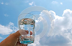 Hand with a glass water in front of blue and white sky