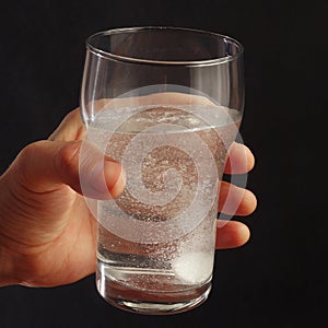 Hand with a glass of water and effervescent pill on dark background.