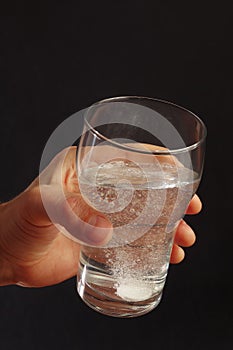 Hand with a glass of water and effervescent tablet on dark background.