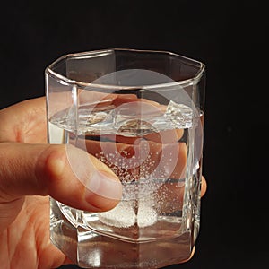 Hand with a glass of water and soluble tablet on dark background.