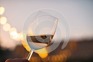 Hand with a glass of white wine checking wine quality at sunset