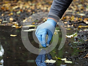 Hand in glove collects water from a puddle in a test tube. Analysis of water purity, environment, ecology - concept