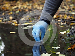 Hand in glove collects water from a puddle in a test tube. Analysis of water purity, environment, ecology - concept
