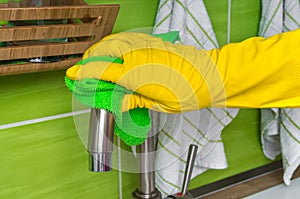 Hand in glove with green rag is wiping faucet in kitchen