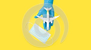 Hand in glove holding model airplanes on yellow background. Airplane model on hand and face medical mask Concept traveling. Copy