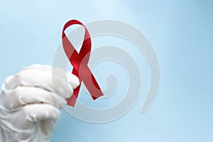 Hand in glove holding a red ribbon, copy space, concept of HIV, AIDS