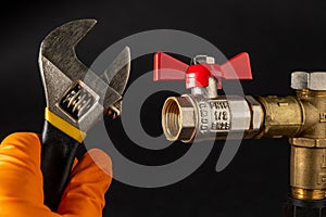 Hand in glove holds an adjustable wrench on the background of plumbing tap. Concept of plumbing repair or gas installation
