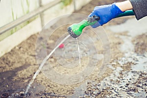 Hand in glove holds watering hose/hand in a rubber protective glove holds a watering, green hose with a green spray nozzle