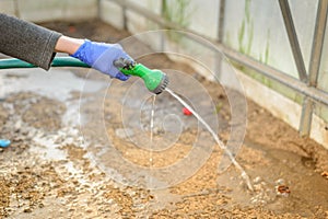 Hand in glove holds watering hose/hand in a rubber protective glove holds a watering, green hose with a green spray nozzle