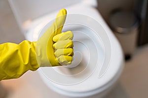 Hand with glove showing thumb up sign against clean toilet