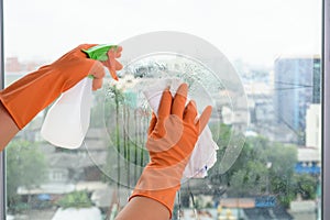 Hand in gloves cleaning window with rag and cleanser spray at ho