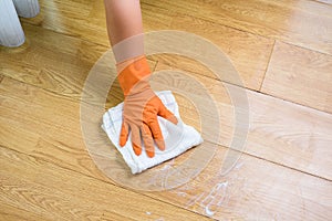 Hand in gloves cleaning Wooden floor with rag and cleanser at
